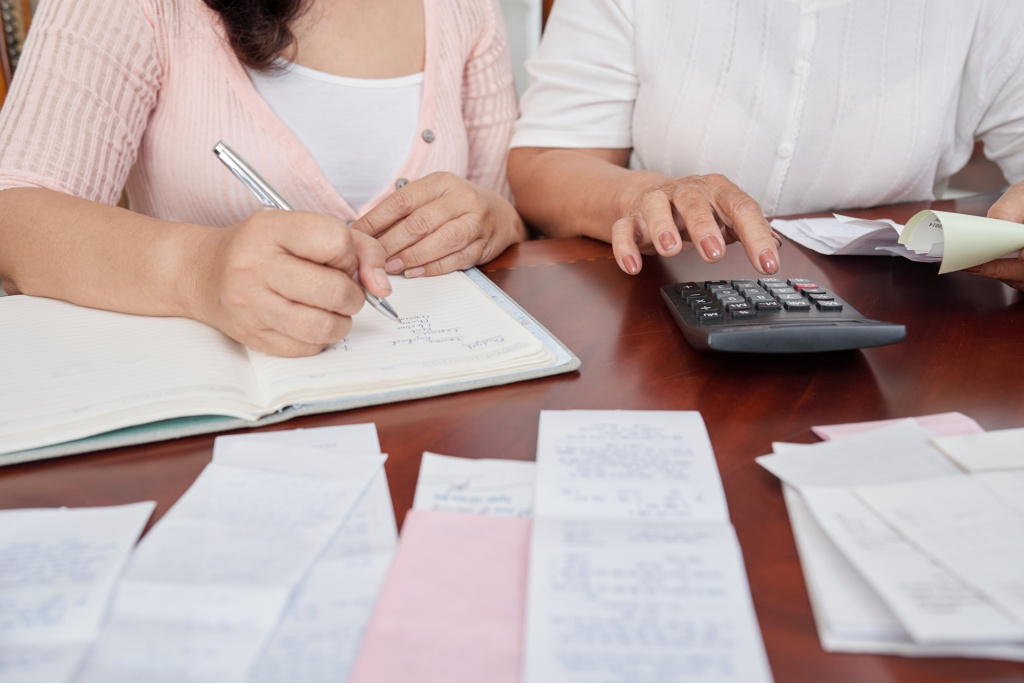 unrecognizable-women-sitting-table-with-receipts-counting-calculator-writing-journal.jpg