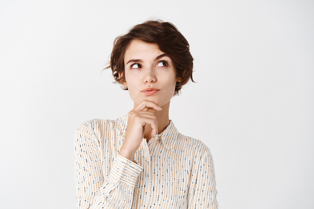 pensive-girl-in-blouse-touching-chin-looking-at-upper-right-corner-and-thinking-making-choice-standing-over-white-wall1.jpg