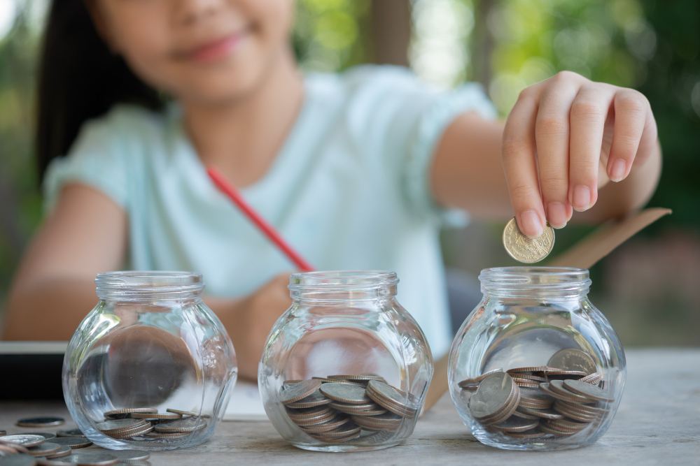 cute-asian-little-girl-playing-with-coins-making-stacks-of-money-kid-saving-money-into-piggy-bank-into-glass-jar-child-counting-his-saved-coins-children-learning-about-for-the-future-concept (1).jpg
